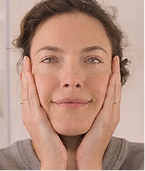 A woman wearing a gray t-shirt cupping her hands in her face.
