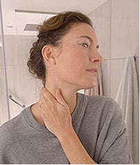 A woman wearing a gray t-shirt massaging product into her neck.