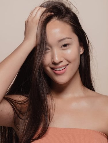 A woman with glass skin holding her hair with one hand